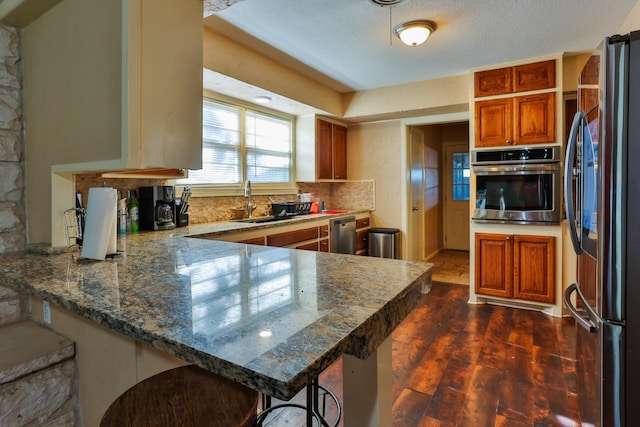 kitchen featuring appliances with stainless steel finishes, kitchen peninsula, a breakfast bar area, and dark stone countertops