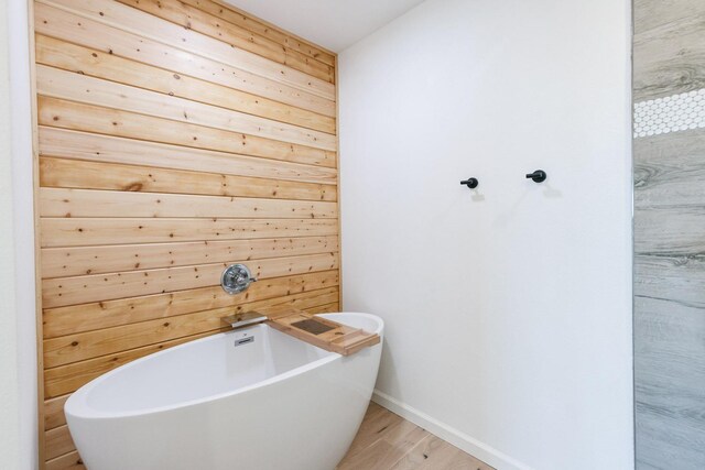 bathroom with a tub to relax in, hardwood / wood-style flooring, and wood walls