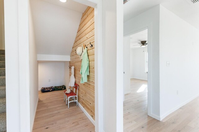 hall featuring vaulted ceiling, light wood-type flooring, and wood walls