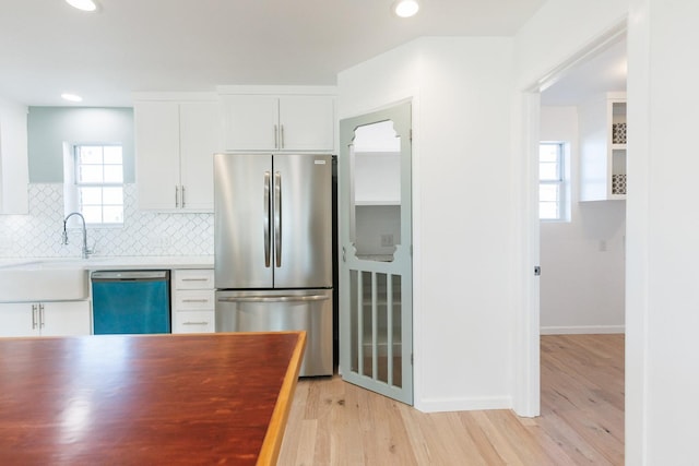 kitchen with sink, light wood-type flooring, stainless steel appliances, decorative backsplash, and white cabinets