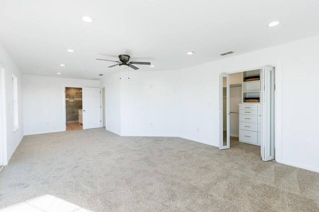 unfurnished bedroom featuring ceiling fan, ensuite bathroom, light carpet, a spacious closet, and a closet