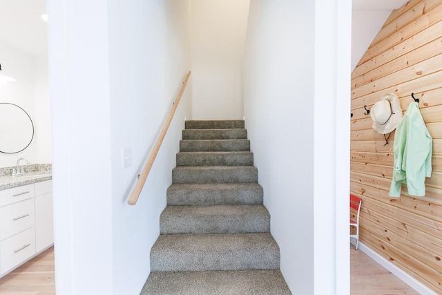 stairs featuring sink, wooden walls, and wood-type flooring