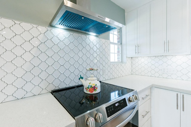 kitchen featuring tasteful backsplash, wall chimney exhaust hood, stainless steel range with electric cooktop, and white cabinets