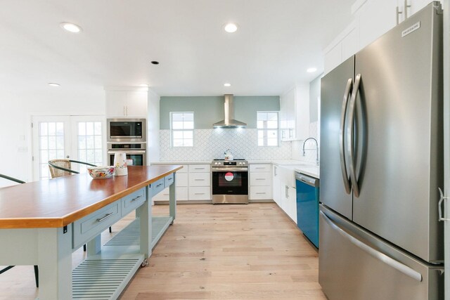 kitchen featuring sink, wall chimney range hood, white cabinets, stainless steel appliances, and backsplash