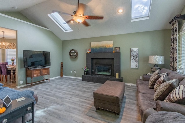 living room featuring hardwood / wood-style flooring, ceiling fan with notable chandelier, vaulted ceiling with skylight, and a fireplace