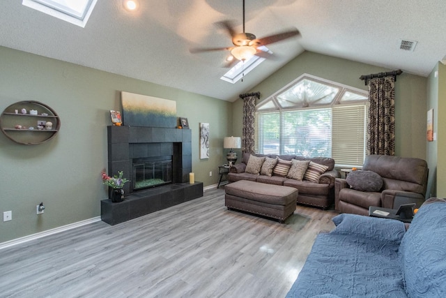 living room featuring lofted ceiling with skylight, a tiled fireplace, light hardwood / wood-style floors, and a textured ceiling