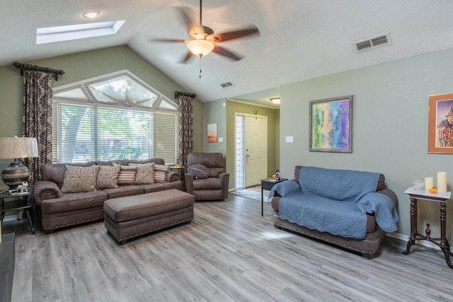 living room featuring vaulted ceiling with skylight, light hardwood / wood-style flooring, and a textured ceiling