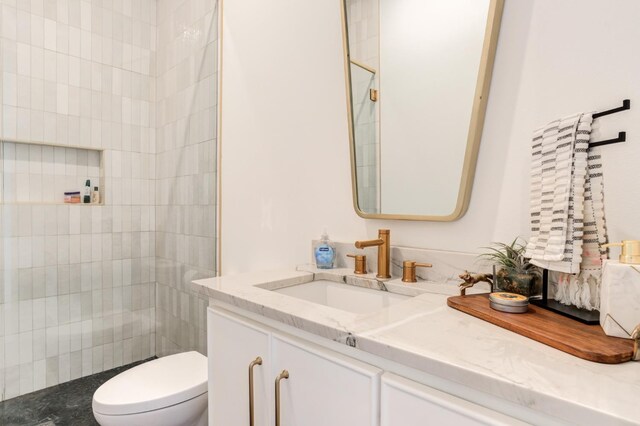 bathroom featuring vanity, toilet, and a tile shower