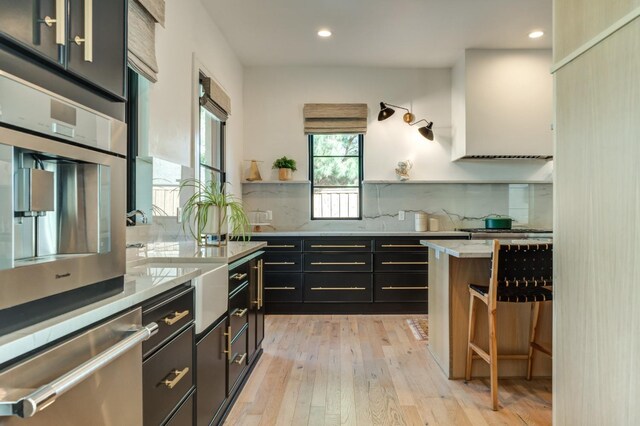 kitchen featuring appliances with stainless steel finishes, wall chimney range hood, light wood-type flooring, and decorative backsplash