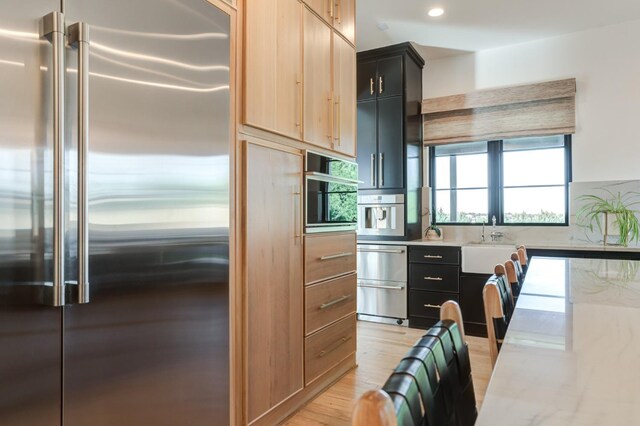 kitchen featuring high end fridge, sink, light hardwood / wood-style flooring, and light brown cabinets