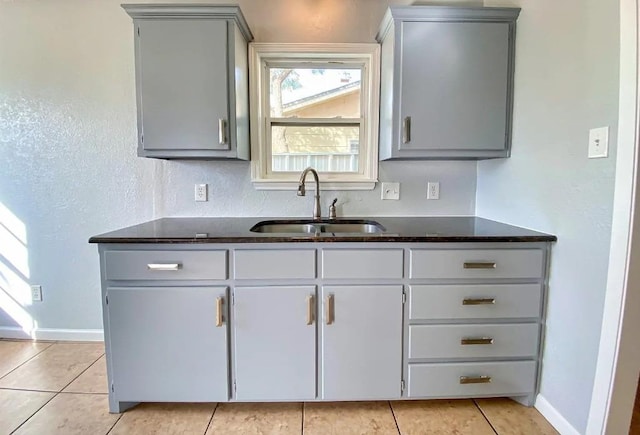 kitchen with sink, gray cabinetry, dark stone counters, and light tile patterned floors