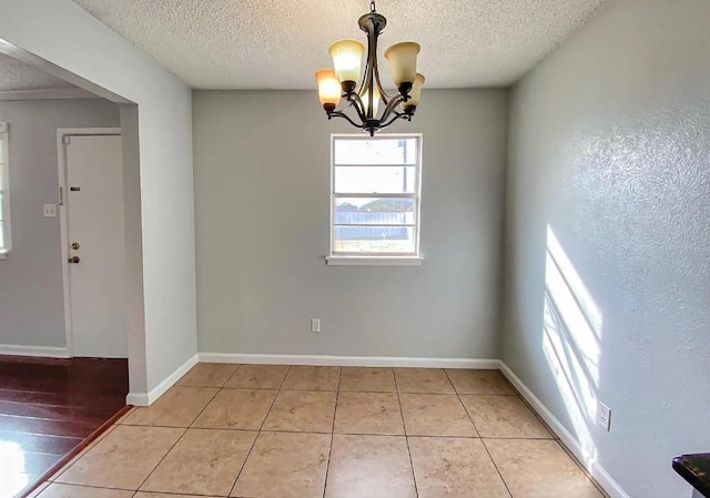 unfurnished dining area featuring an inviting chandelier, tile patterned floors, and a textured ceiling