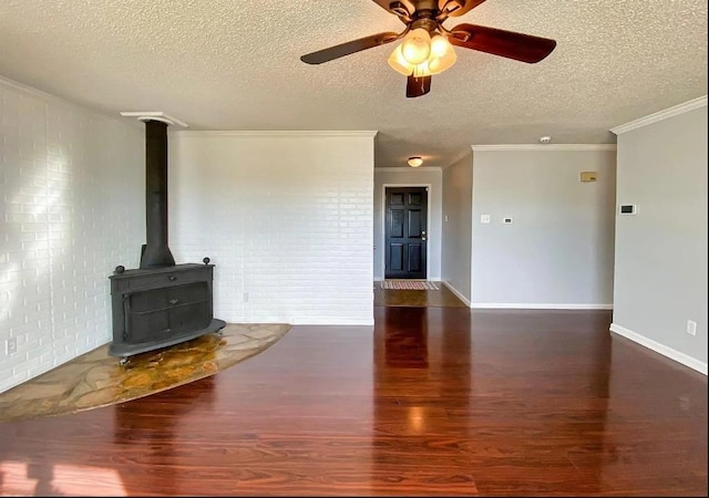 unfurnished living room featuring brick wall, a wood stove, ornamental molding, dark wood-type flooring, and a textured ceiling