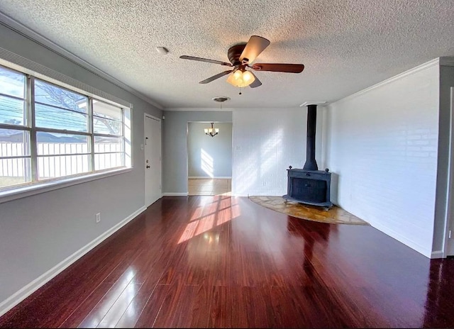 unfurnished living room featuring dark wood-type flooring, a textured ceiling, a wood stove, ornamental molding, and ceiling fan with notable chandelier