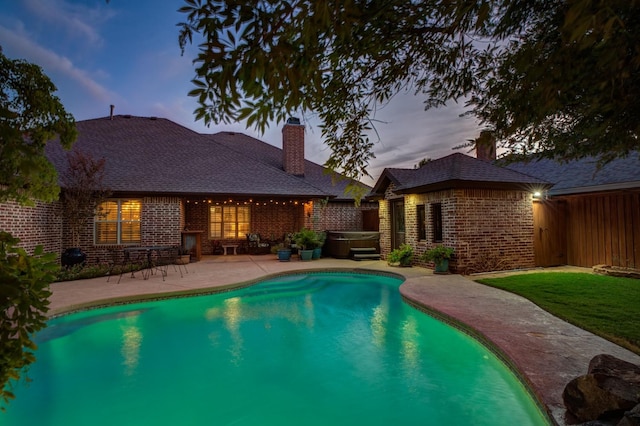 pool at dusk with a hot tub and a patio area