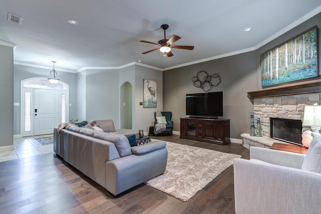 living room with ornamental molding, dark wood-type flooring, ceiling fan, and a fireplace