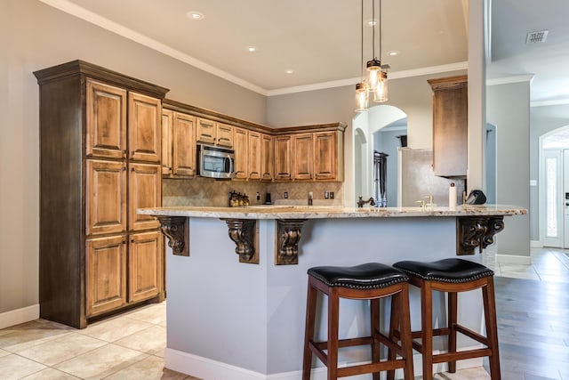 kitchen with crown molding, backsplash, light stone counters, a kitchen bar, and kitchen peninsula