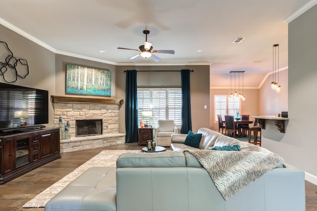 living room with ornamental molding, a stone fireplace, dark wood-type flooring, and ceiling fan