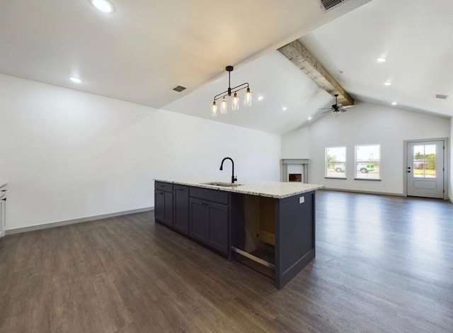 kitchen featuring dark wood-type flooring, sink, light stone counters, decorative light fixtures, and an island with sink