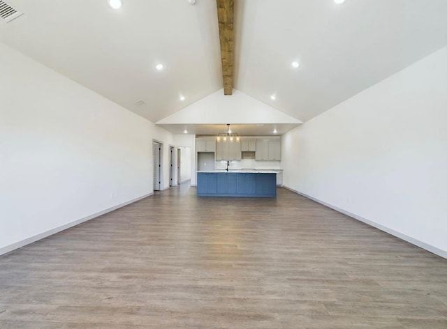 unfurnished living room featuring sink, beam ceiling, high vaulted ceiling, a notable chandelier, and light hardwood / wood-style floors