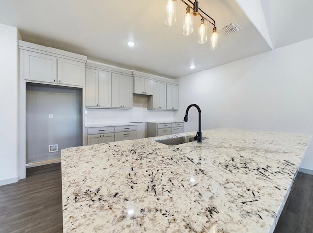 kitchen with a kitchen island with sink, sink, and light stone counters