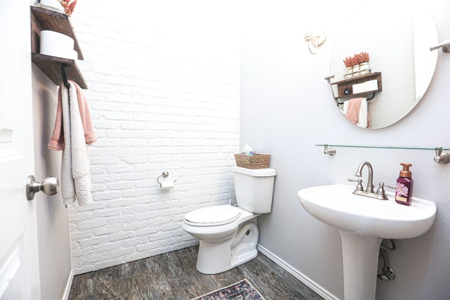 bathroom featuring brick wall, hardwood / wood-style floors, and toilet