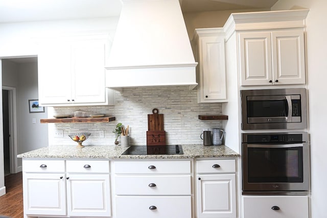 kitchen featuring white cabinetry, light stone counters, premium range hood, and appliances with stainless steel finishes