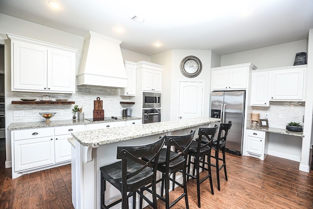 kitchen with premium range hood, a breakfast bar, a center island with sink, appliances with stainless steel finishes, and white cabinets