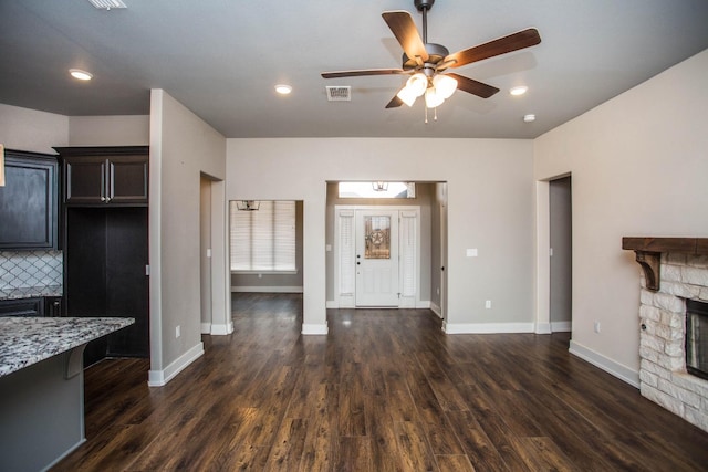 kitchen featuring a fireplace, decorative backsplash, ceiling fan, light stone countertops, and dark wood-type flooring