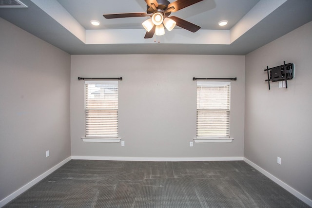 unfurnished room with a tray ceiling, ceiling fan, and dark colored carpet