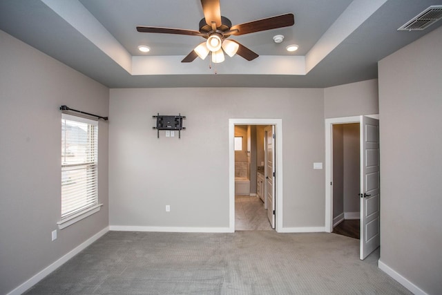 unfurnished bedroom with ceiling fan, ensuite bathroom, a tray ceiling, and light carpet