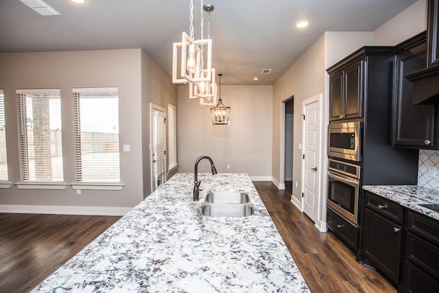 kitchen with pendant lighting, sink, stainless steel appliances, tasteful backsplash, and light stone countertops