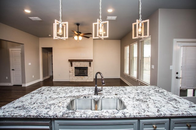 kitchen featuring pendant lighting, a fireplace, sink, a kitchen island with sink, and dark wood-type flooring