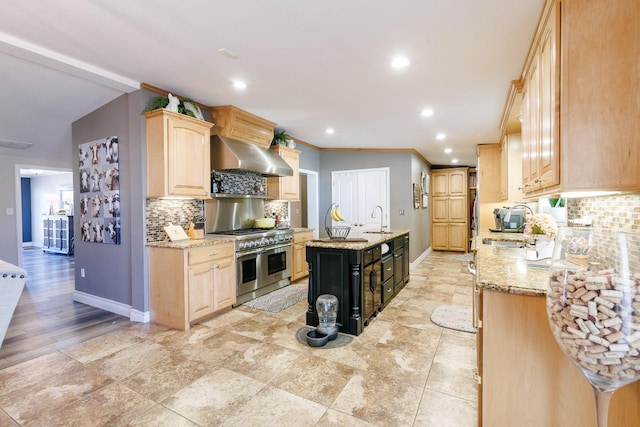 kitchen with light brown cabinetry, a sink, wall chimney exhaust hood, and range with two ovens