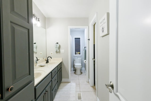 bathroom with baseboards, double vanity, a sink, tile patterned floors, and toilet