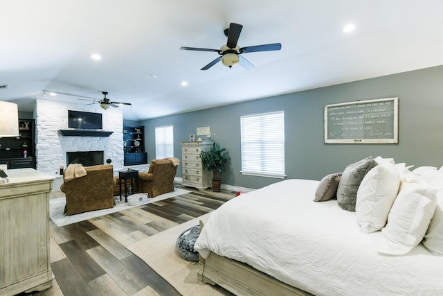 bedroom featuring dark wood-style floors, baseboards, a ceiling fan, a fireplace, and recessed lighting