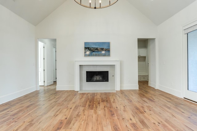 unfurnished living room with a chandelier, high vaulted ceiling, and light hardwood / wood-style flooring