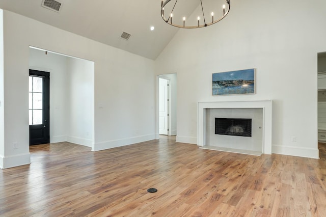 unfurnished living room with a notable chandelier, high vaulted ceiling, and light wood-type flooring