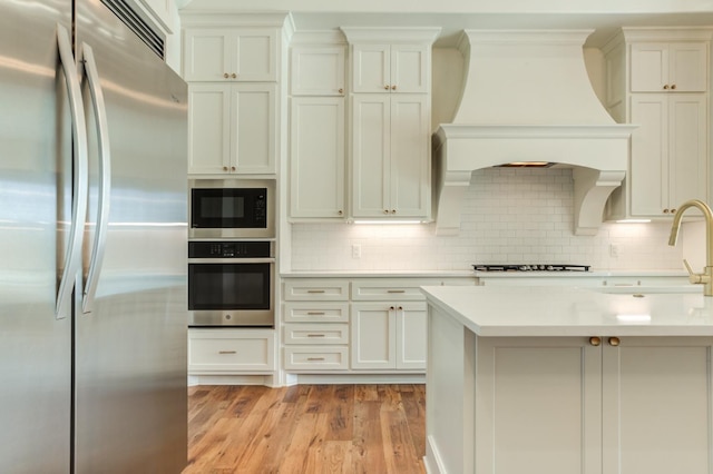 kitchen with decorative backsplash, light hardwood / wood-style flooring, premium range hood, and appliances with stainless steel finishes