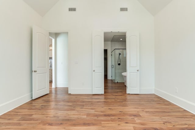 unfurnished bedroom with ensuite bath, high vaulted ceiling, and light wood-type flooring