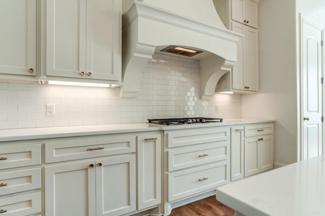 kitchen featuring white cabinets, stainless steel gas stovetop, wood-type flooring, and backsplash