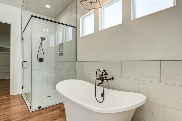 bathroom with hardwood / wood-style flooring, independent shower and bath, a healthy amount of sunlight, and tile walls