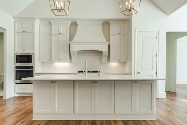 kitchen with premium range hood, built in microwave, stainless steel oven, a center island with sink, and pendant lighting