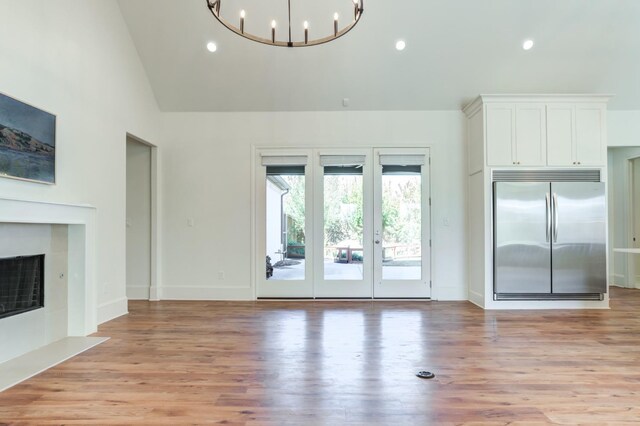 unfurnished living room with a tile fireplace, a notable chandelier, high vaulted ceiling, and light hardwood / wood-style flooring