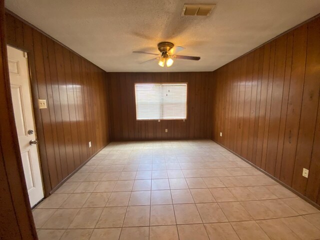 spare room featuring light tile patterned floors, a textured ceiling, wooden walls, and ceiling fan