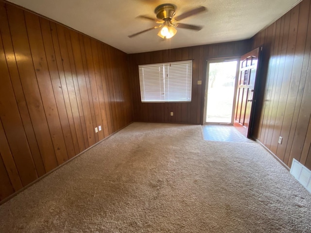 carpeted spare room with a textured ceiling, ceiling fan, and wood walls