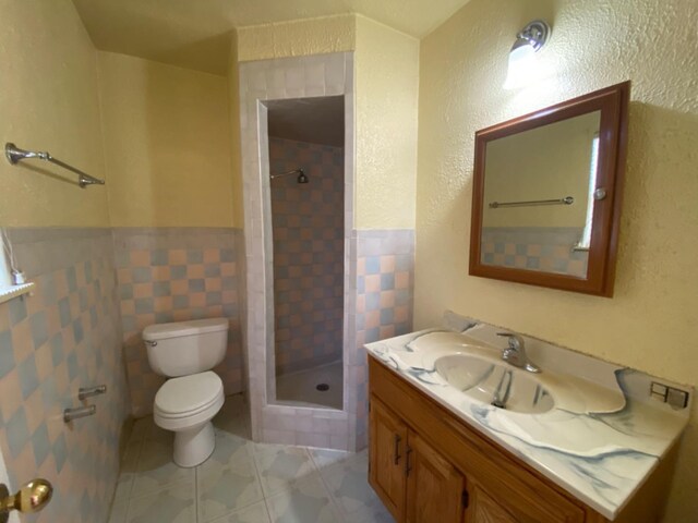 bathroom featuring tile walls, a tile shower, vanity, tile patterned floors, and toilet