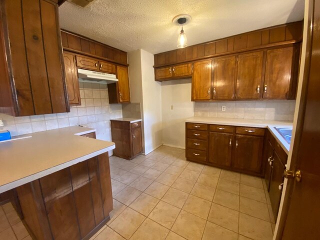 kitchen featuring sink, backsplash, hanging light fixtures, light tile patterned floors, and a textured ceiling