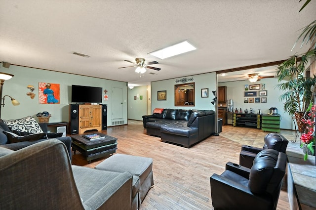 living room featuring ceiling fan, a skylight, light hardwood / wood-style flooring, and a textured ceiling