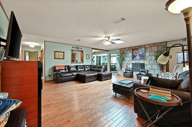 living room featuring ceiling fan, light hardwood / wood-style floors, and a textured ceiling